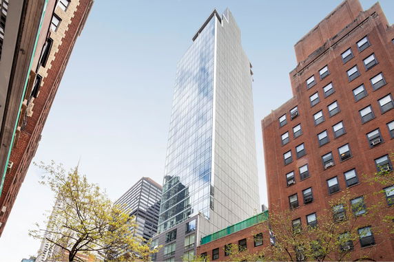 Tall glass-fronted skyscraper with adjacent brick buildings.