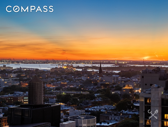 Panoramic view of a cityscape at sunset, overlooking buildings and a waterway.