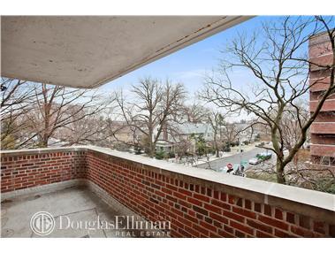 View from a brick balcony overlooking a residential street with trees and buildings.