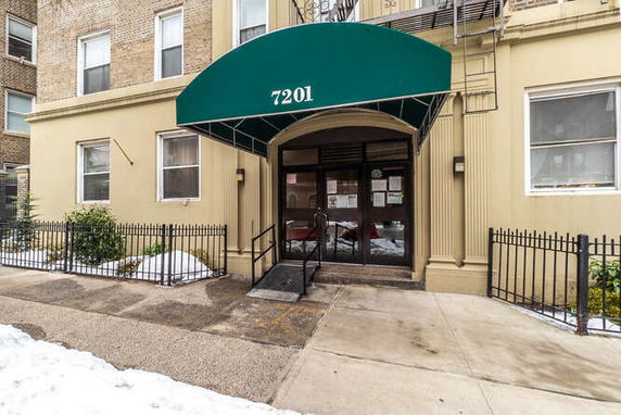 Front view of an apartment building entrance with a green canopy and brick facade.