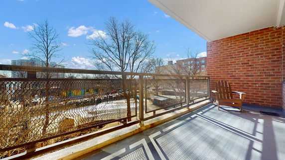 Balcony view with metal railing and brick wall overlooking trees and buildings in the background.