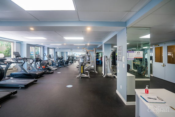Indoor gym area with various exercise equipment and large windows.