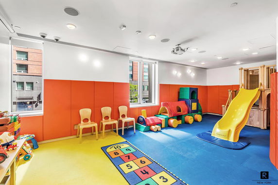 Indoor children's play area with colorful mats, slide, and play structures.
