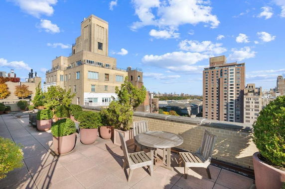 Rooftop terrace with potted plants and seating area overlooking surrounding buildings.