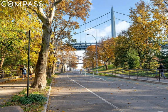 View of a tree-lined path with a bridge in the background, during autumn.