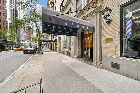 Front view of an urban building entrance with an awning displaying '142 E 49TH'.