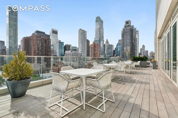 Rooftop terrace with tables and chairs overlooking a city skyline.