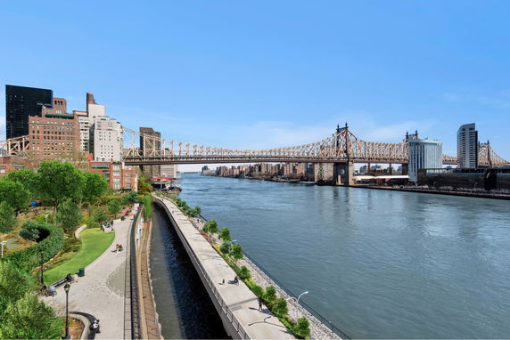 View of a river with a bridge, buildings on one side, and a green park area with walkways.