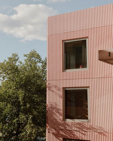 Front view of a modern building with pink textured facade and windows.