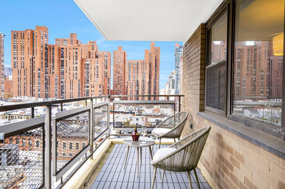 Balcony view with outdoor seating facing tall brick buildings.