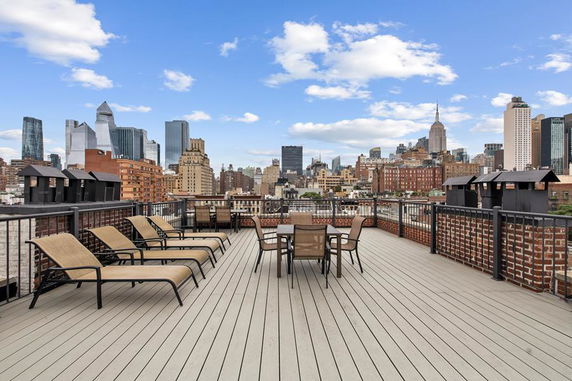 Rooftop deck with lounge chairs and table set, overlooking a city skyline.