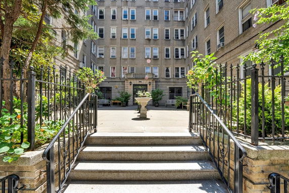 Front view of a multi-story residential building with a courtyard and stairs leading to the entrance.