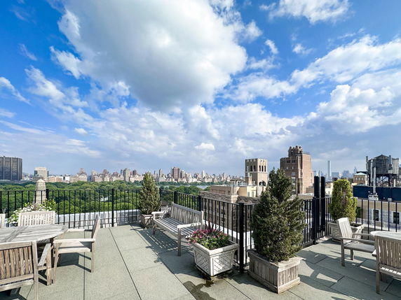 Rooftop with seating and planters, offering a view of city buildings and green park area.
