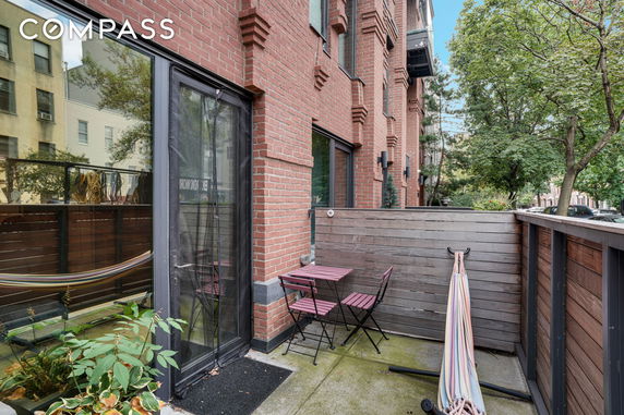View of a brick building with patio area featuring small outdoor furniture and a glass door entrance.