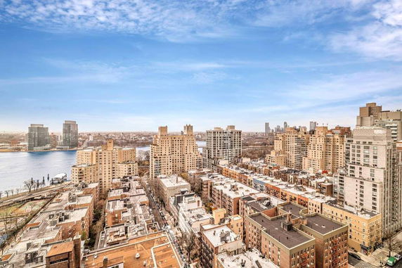 Panoramic view of a city skyline with river, tall buildings, and cloudy sky.