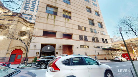Front view of a multi-story building with a street and parked cars.