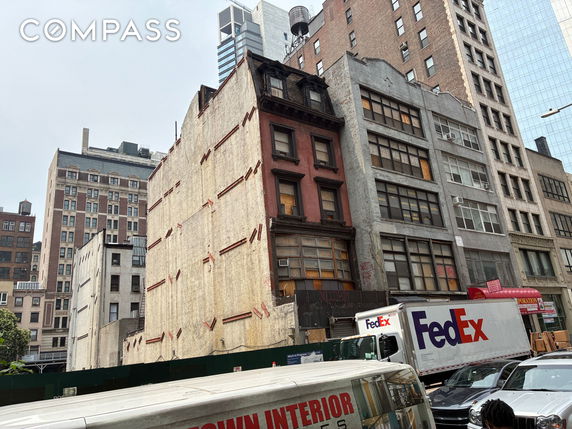 Front view of a multi-story urban building with various architectural styles and a delivery truck in front.