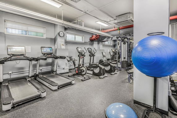 Room with gym equipment including treadmills, exercise bikes, and a stability ball.