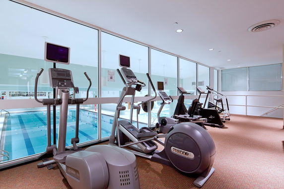 Indoor gym area with exercise machines overlooking a pool.