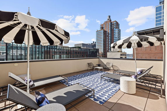 Rooftop area with lounge chairs, umbrellas, and views of surrounding buildings.
