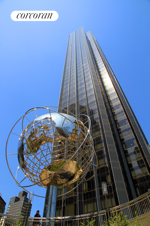 Front view of a tall skyscraper with reflective windows and a globe sculpture in the foreground.