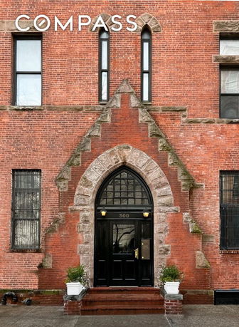 Front view of a brick building entrance with arched doorway and windows.