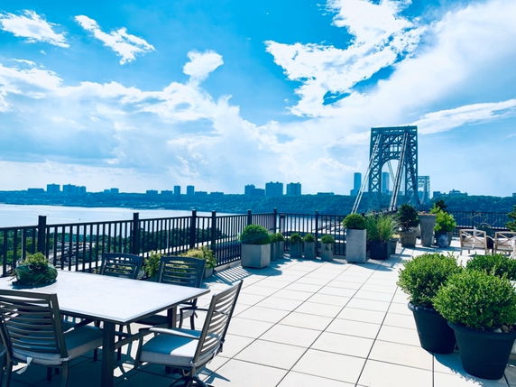 Rooftop view featuring seating and potted plants with a cityscape and bridge in the background.