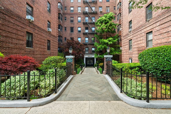 Front view of a brick apartment building with a landscaped entrance walkway.