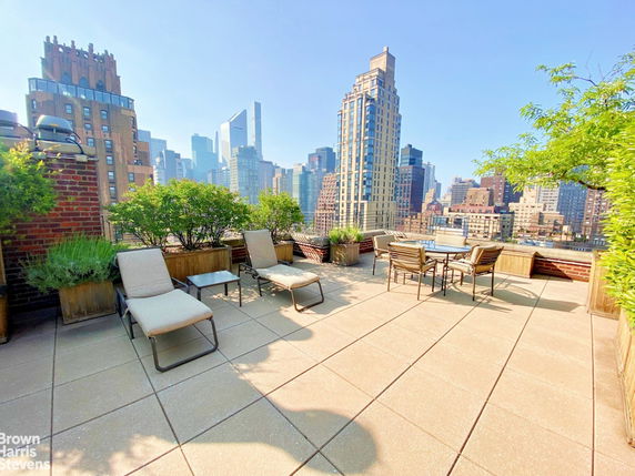 Rooftop terrace with seating and greenery, overlooking city skyline.