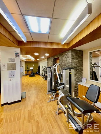 Interior view of a gym area with exercise machines and wooden flooring.