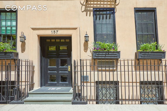 Front view of a building with a black door and window boxes with flowers.