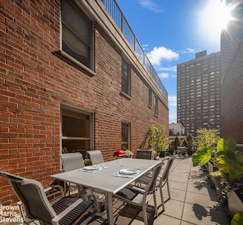 View of a rooftop area with outdoor seating and potted plants, surrounded by brick building walls.