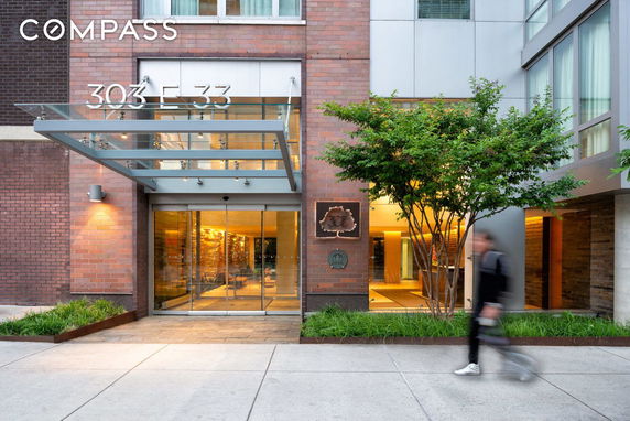 Front view of a brick building entrance with glass canopy and sliding doors.