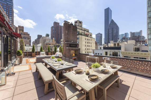 Rooftop patio with dining area and city skyline view, featuring outdoor furniture and a fireplace.