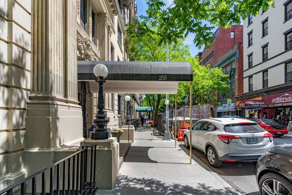 Front view of a building entrance with an awning and decorative columns on a street with parked cars.