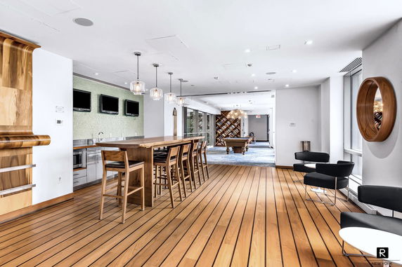 Room with a long wooden table, bar stools, flat-screen TVs, and a pool table in the background.