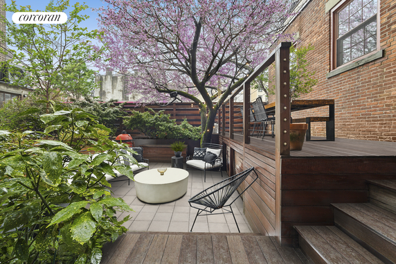Outdoor patio area with seating, wooden deck, and flowering tree.