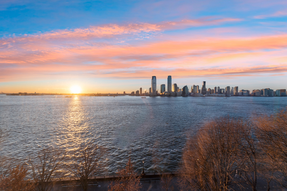 Panoramic view of a city skyline across a body of water during sunset.