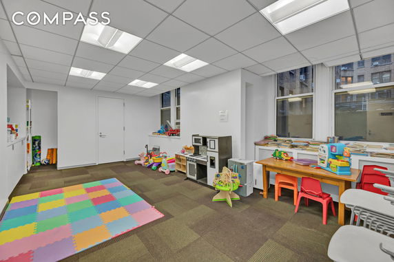 An indoor play area with colorful foam mats, small tables, chairs, and children's toys.