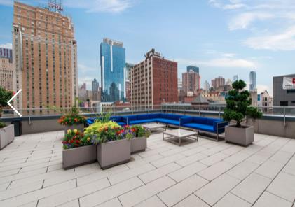 Rooftop area of a building with seating and planters, surrounded by cityscape.