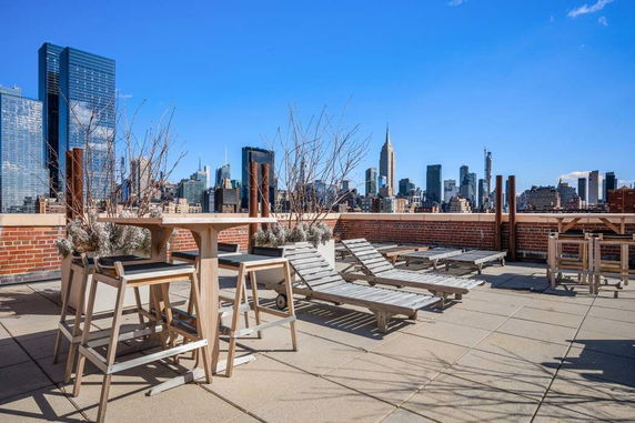 Rooftop with lounge chairs and tables, featuring a view of a city skyline.
