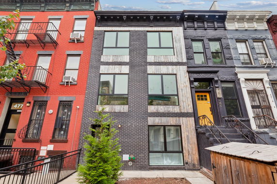 Front view of a three-story urban townhouse with a modern facade featuring large windows and a mix of brick and wood siding.
