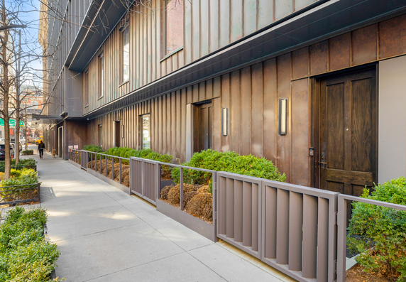 Street-level view of a modern apartment building with metal paneling and landscaped entrance.