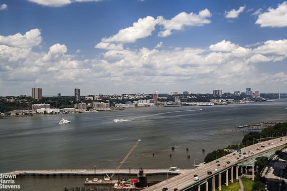 Panoramic view of a river with boats and distant buildings under a blue sky.