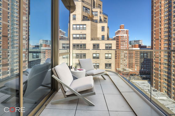 Panoramic view from a balcony with outdoor seating, overlooking city buildings.