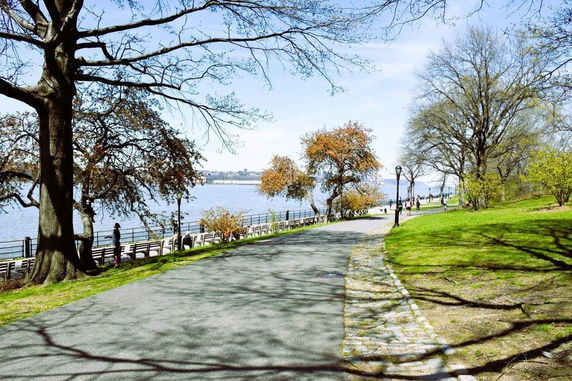 Pathway alongside a river with trees and grass, people walking in the distance.