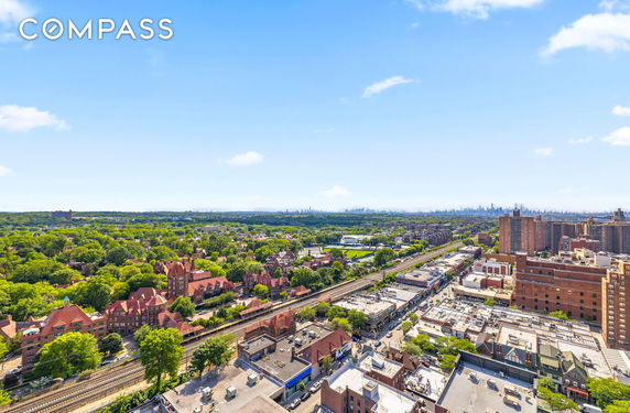 Panoramic view of a cityscape with residential and commercial buildings, train tracks, and greenery.