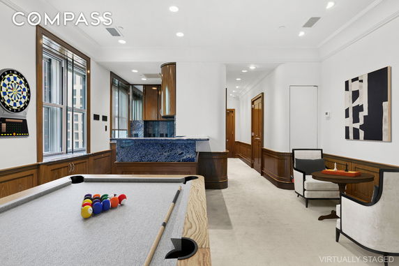 Interior view of a room with a pool table, dartboard, and seating area with a small table and chairs next to a bar.