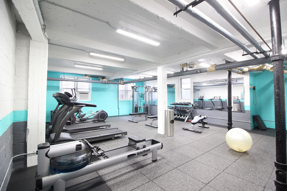 Interior view of a gym with exercise equipment and bright turquoise walls.