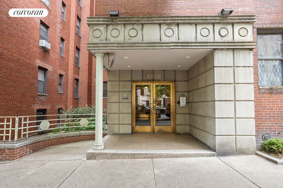 Front view of a multi-story brick building entrance with columns and double doors.
